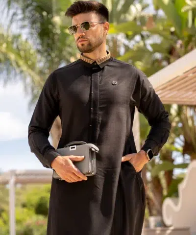 Homme aux cheveux châtains portant des lunettes de soleil et un sac à main noir vêtu d'un fantastique qamis al ameer aar2408 noir.
