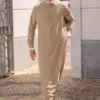 Homme chauve avec une barbe et des lunettes de soleil pourtant un magnifique qamis al ameer aar2423 beige.