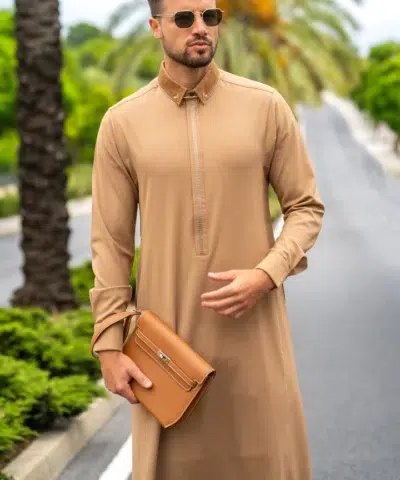 Homme aux cheveux chatains avec des lunettes de soleil et une petite barbe portant une magnifique qamis al ameer aar2425 marron clair avec une sacoche marron.